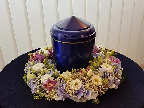 Urne funéraire bleue nuit entourée d'une couronne de fleurs pour cérémonie de crémation