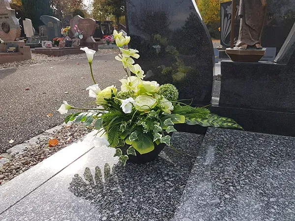Composition florale posée sur une stèle en granit dans un cimetière pour une inhumation