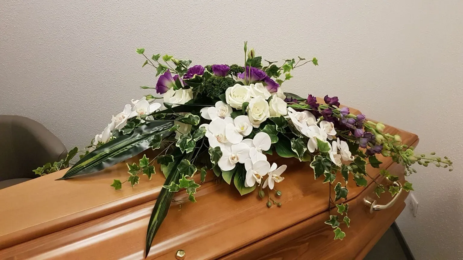 Cercueil en bois orné d'une composition florale de lys blancs et fleurs violettes