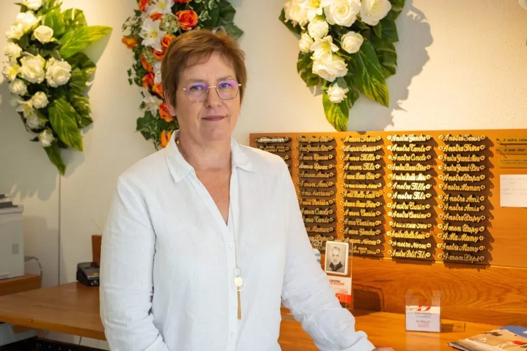 Conseillère funéraire posant devant un présentoir de rubans de deuil et des compositions florales